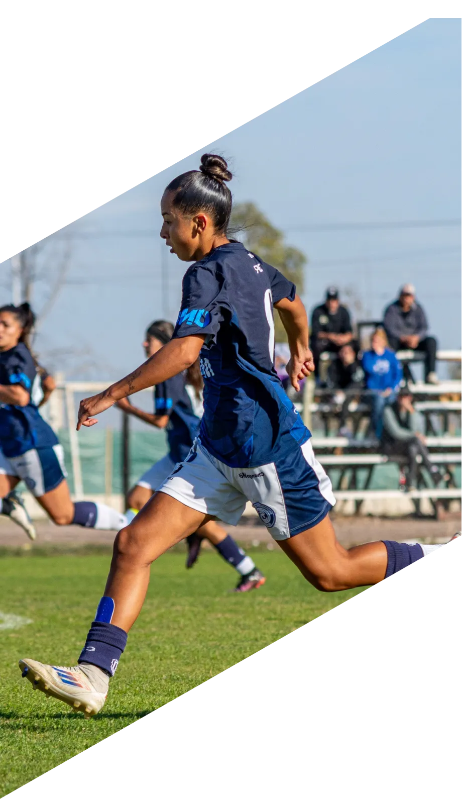 A young player striking a ball during a training session, with teammates and coaches watching from behind.