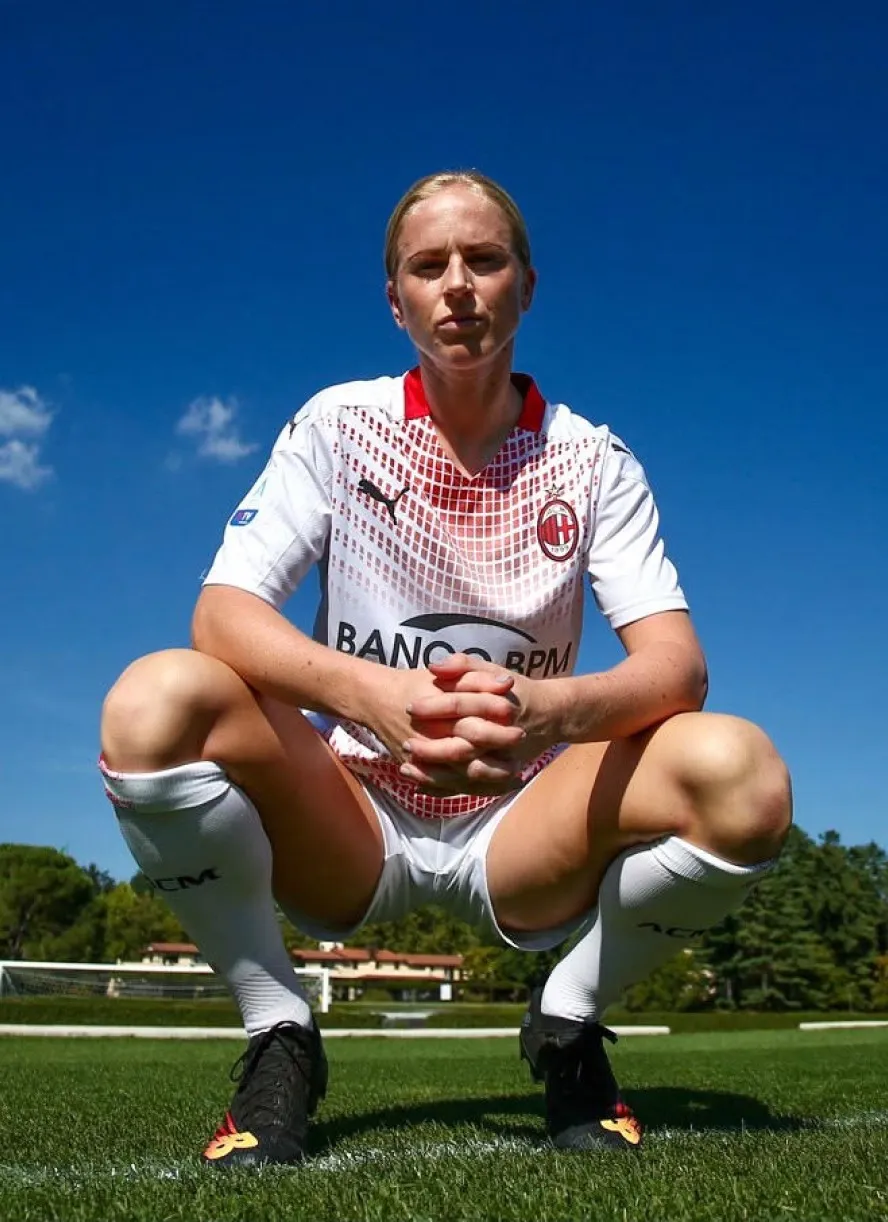 Natasha Dowie crouching on a training pitch in a white kit, hands clasped, looking straight at the camera.