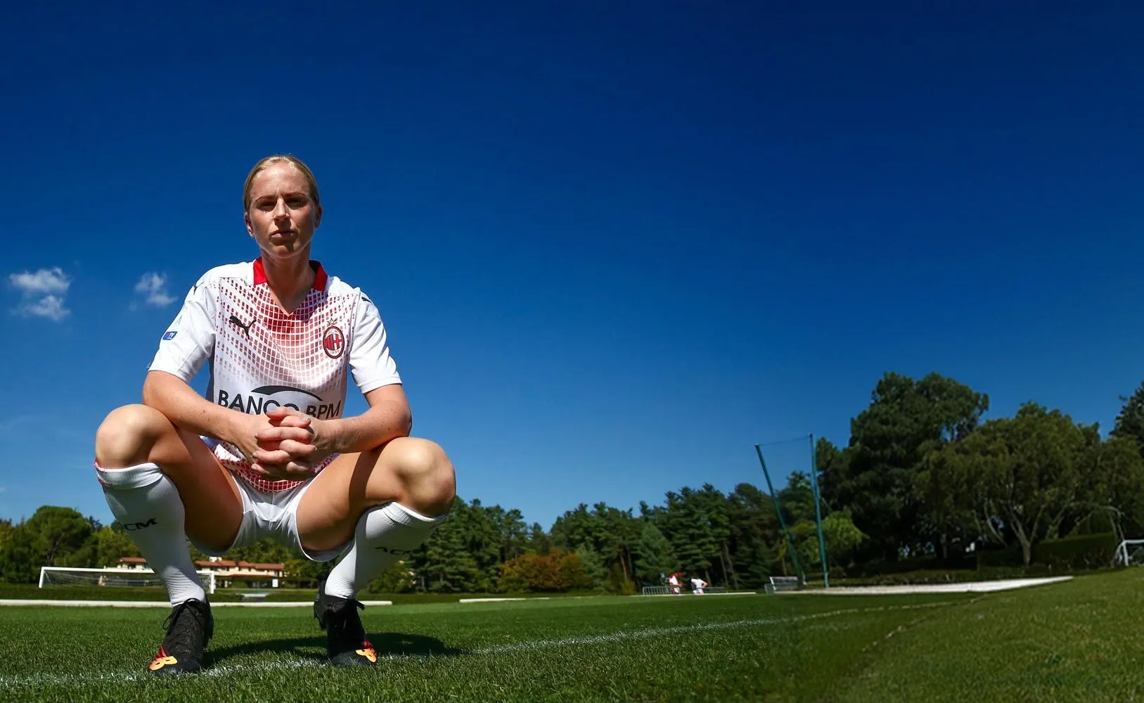 Natasha Dowie crouching on a training pitch in a white kit, hands clasped, looking straight at the camera.