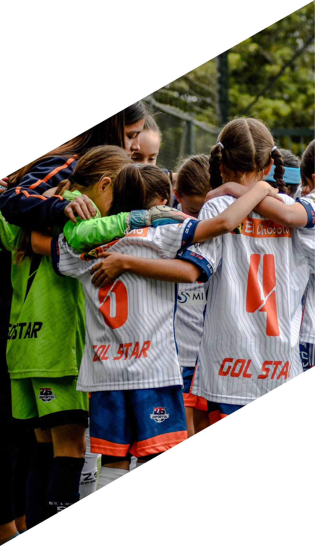 A girls' team huddled together with their arms around each other, seen close in from one side.